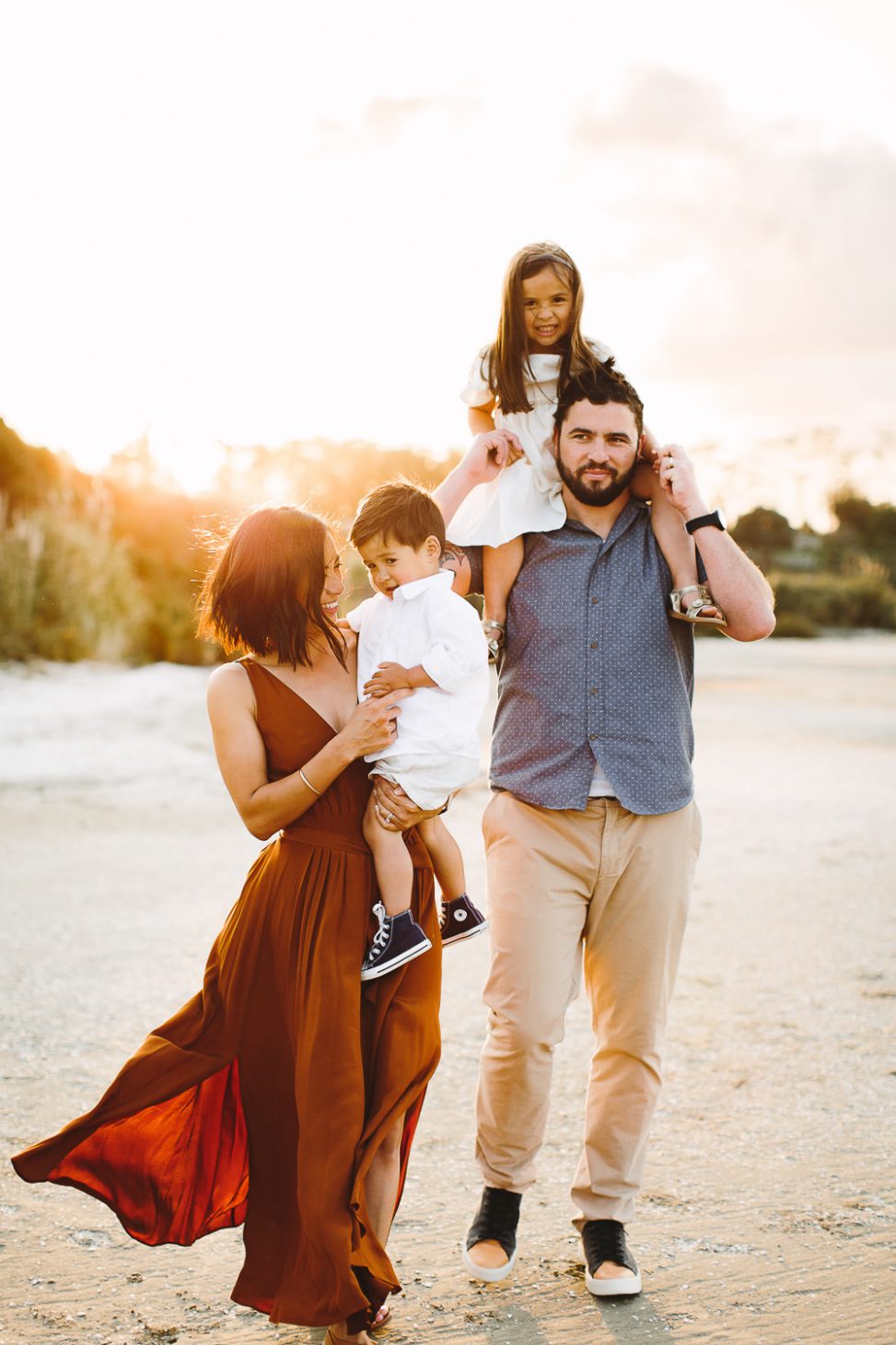 Family of four at beach, mother holding toddler and father with daughter on shoulders